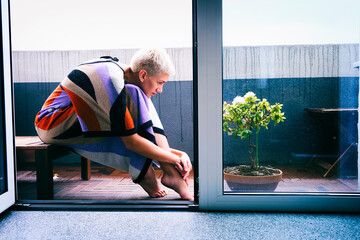 blonde woman in a dress with a color print is sitting on the balcony on a summer day talking to a...
