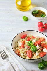 Warm salad of boiled pearl barley, ripe tomatoes, feta cheese with pesto sauce in a white plate on a light wooden background.
