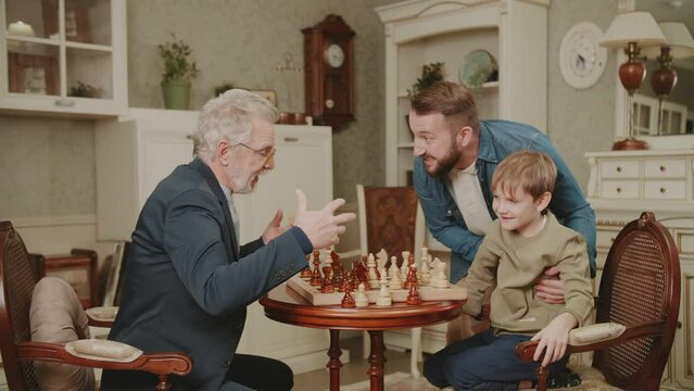 The grandson puts a checkmate to the grandfather. Dad is happy and proud of his son. Three generations of men from the same family play chess at home. A family hobby. The story of one family.