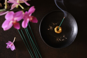 Overhead view of burning japanese incense stick with smoke on round black holder and pink orchid flowers