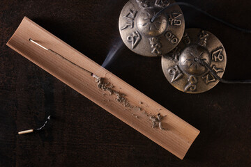 Overhead view of burning incense stick and ritual tibetan cymbals with engraved sanskrit mantra...