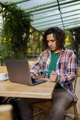 Hispanic young man outdoors with laptop online shopping