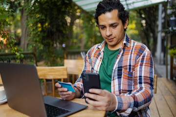 Hispanic young man outdoors with laptop and mobile phone online shopping
