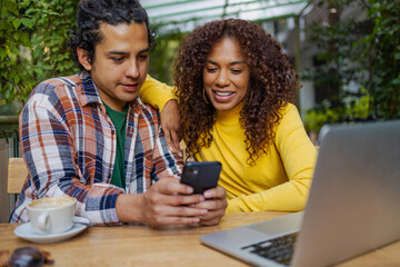 Attractive young multiethnic couple outdoors using mobile phone and laptop