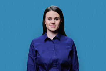 Fototapeta premium Smiling young woman looking at camera on blue background