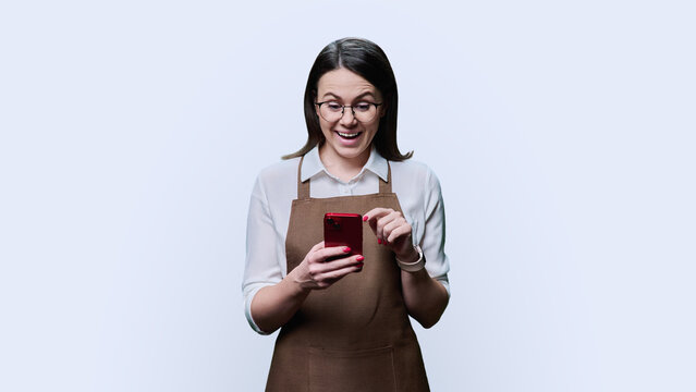 Young smiling woman in apron looking at smartphone, on white background