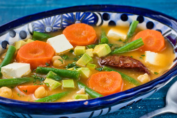 青背景の伝統的なメキシコのスープ　カルド・トラルペーニョ　チレ・チポトレを添えて　Traditional Mexican soup Caldo Tlalpeño with chile chipotle on blue background