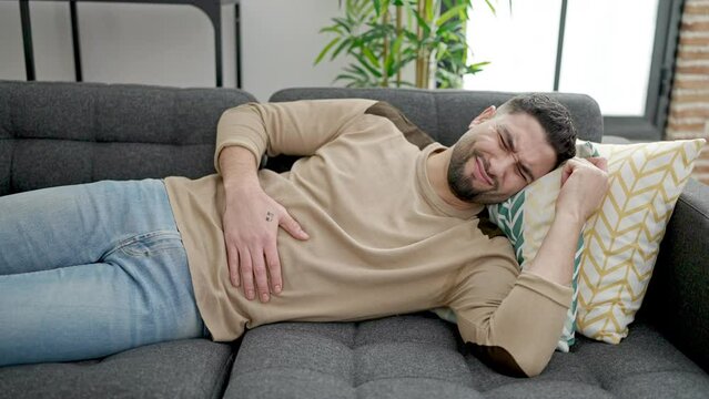 Young arab man suffering for stomach ache lying on sofa at home