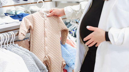 A woman chooses children's clothes in a children's clothing store. Pregnancy and shopping