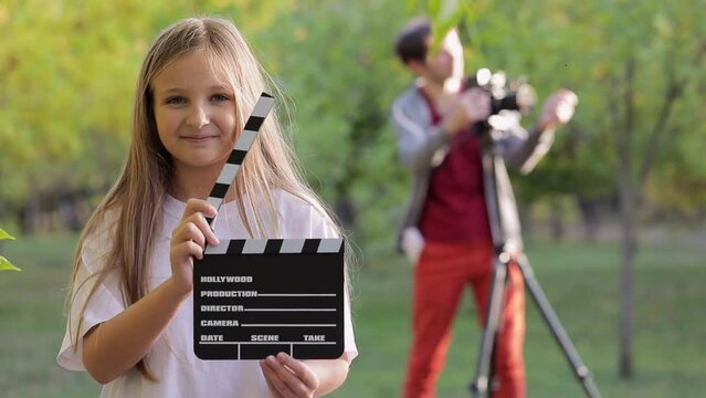 A little girl holds a movie clapperboard in her hands and clap it, the children shoot the whole movie