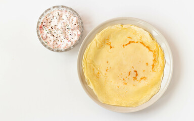 Pancakes on a plate. Sauce with tomatoes and sour cream in a bowl. Top view.