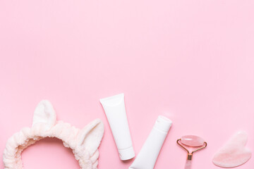 Face care concept. Asian Gua Sha massage tools, cream, mask in white plastic tubes, hair band on light pink background with copy space for your design.