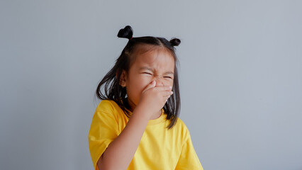 Image of little Asian child wearing yellow tshirt sneeze on gray background.