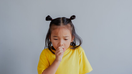 Image of little Asian child wearing yellow tshirt sneeze and cough on gray background.