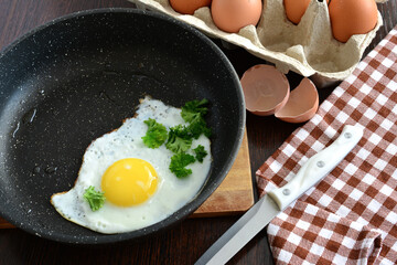 fried egg with yellow yolk on black frying pan isolated with eggshells on background