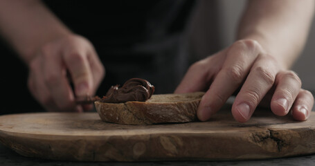 man spreading chocolate hazelnut spread on ciabatta slice on wood board