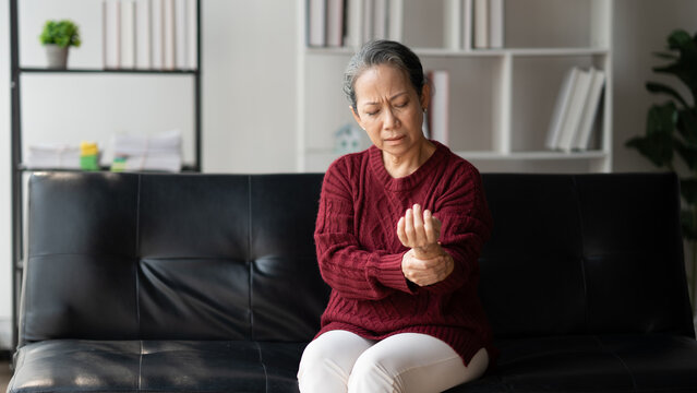 Unhappy 60 years old Asian woman holding wrist, suffering from strong pain in hand.