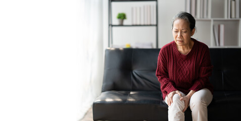 Fototapeta premium Senior woman suffering from pain in knee in the living room at her home.
