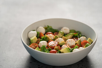 Salad with avocado, tomatoes and mozzarella in white bowl