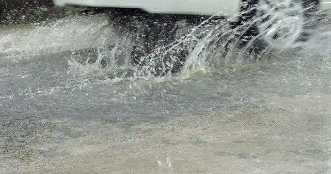 Water flow at road surface, automobile pass by with splash from wheels. Slow motion shot in heavy rain. Typical weather at rainy season on Bali. Small town streets flooded with running water