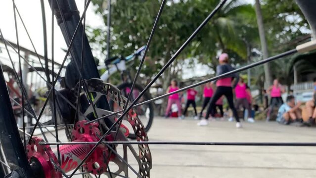 Zumba dancers sway obscured by the view of bicycle brakes. Blurs selective focus