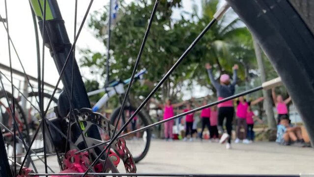 Zumba dancers sway obscured by the view of bicycle brakes. Blurs selective focus