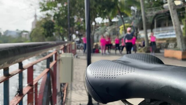 Zumba dancers sway obscured by the view of bicycle seat. Blurs selective focus