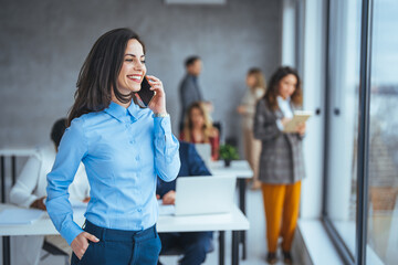 Shot of a young businesswoman using a cellphone in an office. Shot of an attractive young businesswoman using a smartphone in a modern office. Smiling business woman in casuals talking on phone....