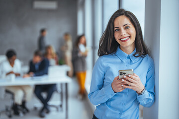 Smiling businesswoman using phone in office. Small business entrepreneur looking at her mobile...