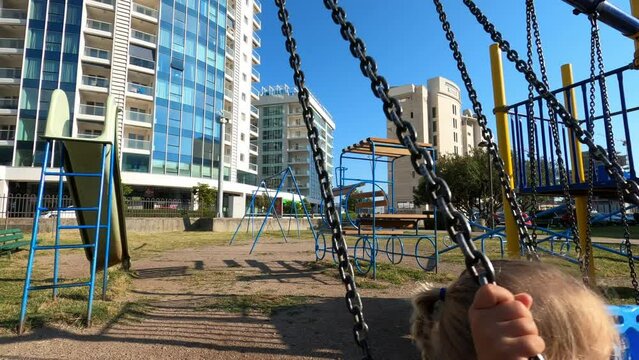 Little girl swings on a swing at the playground near skyscrapers