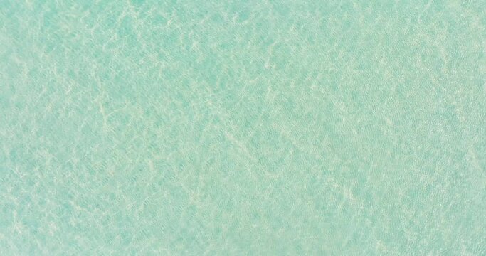 Water texture background Cinematic The clear water surface of the tropical sea reflects the sunlight, overlooking the white sand beneath the pure beauty of nature. Footage high quality 4K ProRes 422HQ