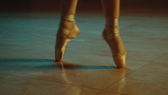 Cinematic close up shot of classical ballet dancer feet in pointe shoes. Female dancer on choreography rehearsal in opera. Professional ballerina trains moves before start a show. Graceful ballet art.