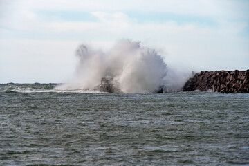 Fototapeta na wymiar Massive wave hits a small lighthouse on a jetty