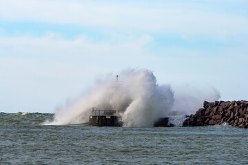 Fototapeta na wymiar Massive wave hits a small lighthouse on a jetty