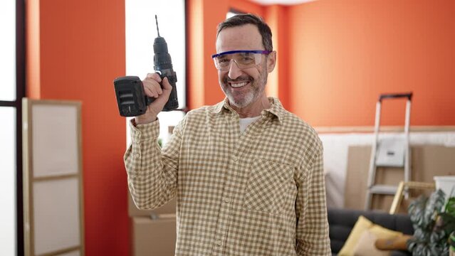 Middle age man wearing security glasses holding drill at new home