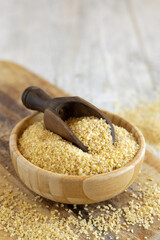 Raw Dry bulgur wheat grain in a wooden bowl with a scoop close up, copy space