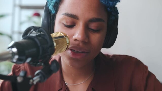 Young upset African American woman pursing lips uses microphone to read out important information about emergency or obituary sits at table with papers and cup of coffee in studio. Radio, podcasting