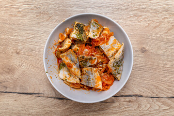 Raw herring in oil with paprika and cucumber, standing in a white plate on table.