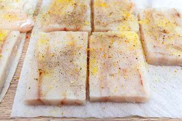 Fresh cod fillet cut into squares, sprinkled with spices lying on a paper towel, top view.