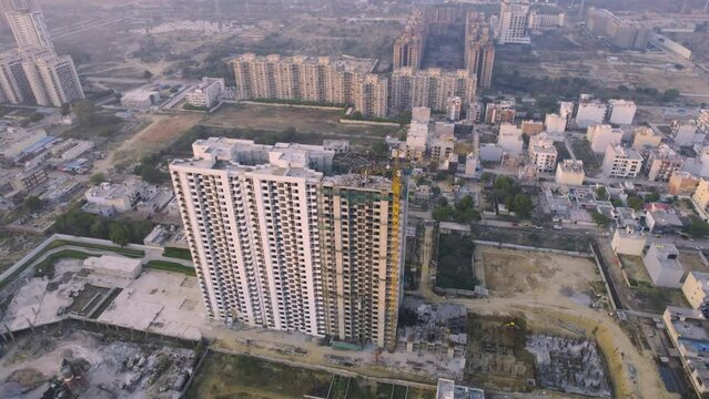 Aerial drone shot rotating around under construction building with barren land nearby and lots of small houses and shops in the distance showing real estate property development