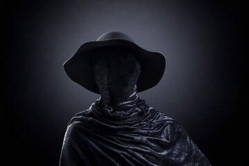 Creepy figure with old hat over dark misty background