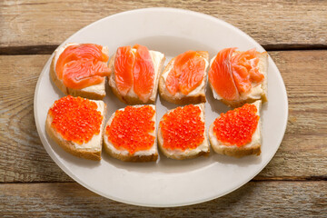Naklejka na ściany i meble Toasts with red caviar and salted trout and butter on a plate on a wooden table.