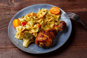 Pasta with vegetables and cherry tomatoes with baked chicken leg on the table