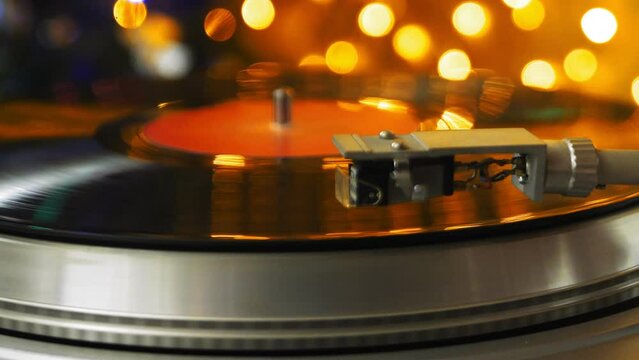 Retro turntable with vinyl records and a needle on the background of Christmas lights spins the record. Medium plan.