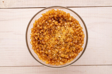 Yellow gelatin granules in a glass plate on a wooden table, macro, top view.