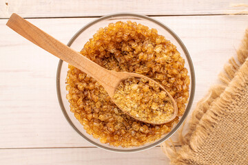 Yellow gelatin granules in a glass plate with a wooden spoon on a wooden table, macro, top view.