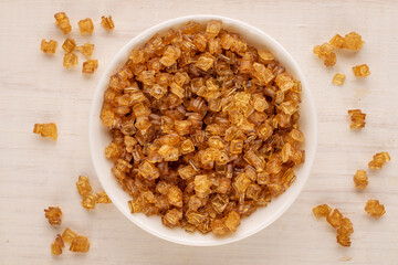 Yellow gelatin granules in a white ceramic plate on a wooden table, macro, top view.