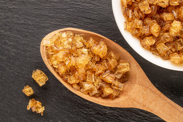 Yellow gelatin granules in white plate with wooden spoon on slate stone, macro, top view.
