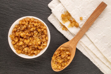 Yellow gelatin granules in white plate with wooden spoon and white napkin on slate stone, macro, top view.