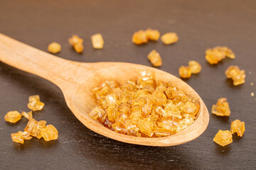 Yellow gelatin granules with wooden spoon on slate stone, macro.